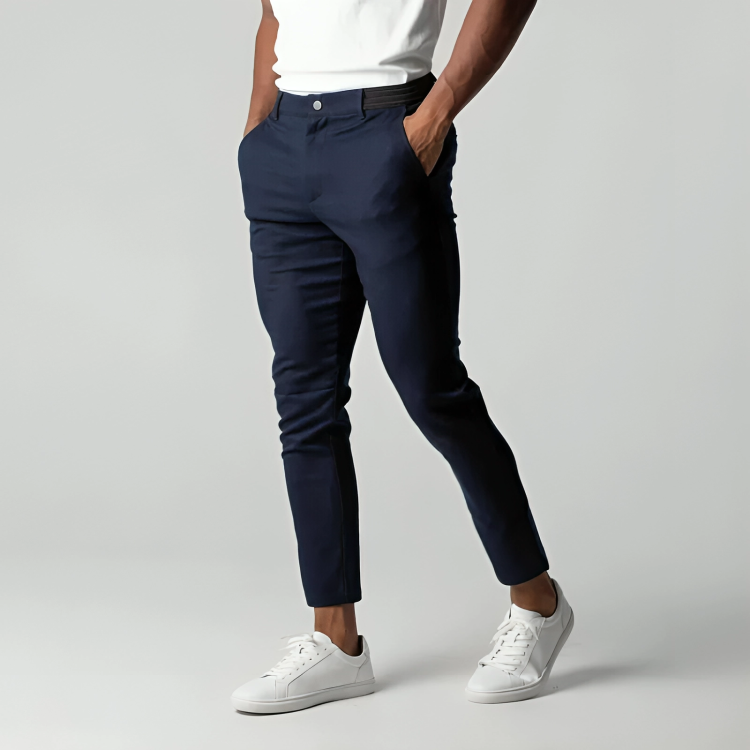 Mann in dunkelblauer Chinohose und weißen Sneakern, Hände in den Hosentaschen, vor grauem Hintergrund. Elegante Herrenmode, Freizeitlook.