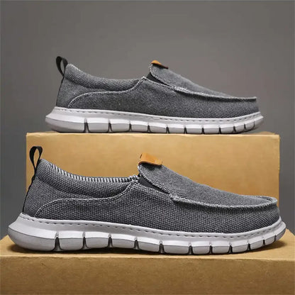 Graue Herren-Sneaker aus Stoff mit weißer Sohle, präsentiert auf einem Karton. Bequeme, modische Freizeitschuhe für Alltag und Sport.