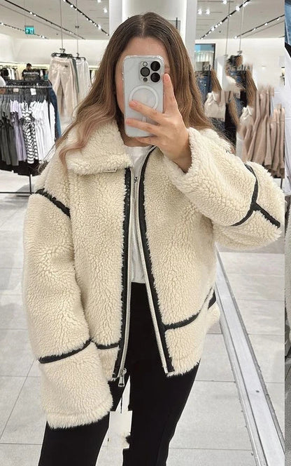 Frau in weißer Teddyjacke mit schwarzen Streifen macht Selfie im Bekleidungsgeschäft. Modetrend, Wintermode, Damenjacke, Shopping.