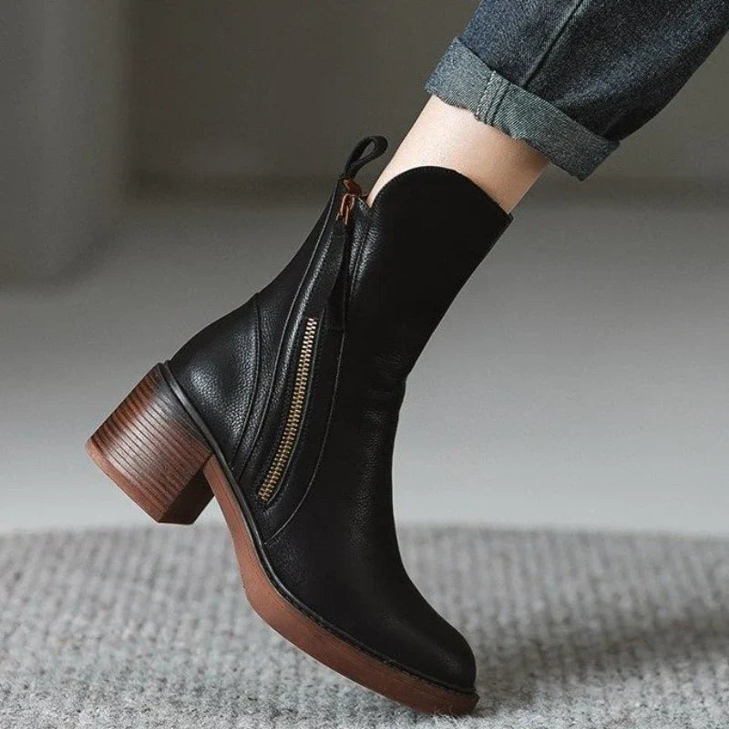 Schwarzer Lederstiefel mit Reißverschluss und Blockabsatz, getragen von Person in Jeans. Modischer Damenstiefel, Herbst-Winter-Schuhtrend.