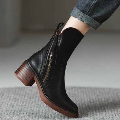 Schwarzer Lederstiefel mit Reißverschluss und Blockabsatz, getragen von Person in Jeans. Modischer Damenstiefel, Herbst-Winter-Schuhtrend.
