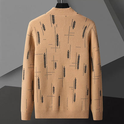 Beiger Pullover mit schwarzem Blattmuster, geometrischem Design, hängend auf einem Kleiderbügel vor grauem Hintergrund. Modischer Strickpullover.