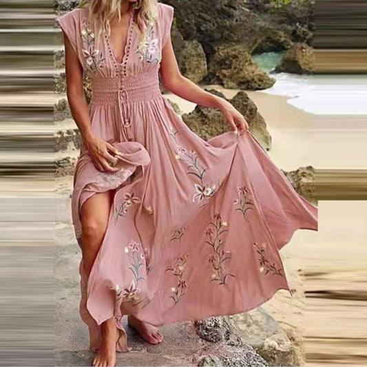 Frau in rosa Sommerkleid mit Blumenstickerei am Strand, fließender Stoff, Boho-Stil, ideal für Strandmode und Sommeroutfits.