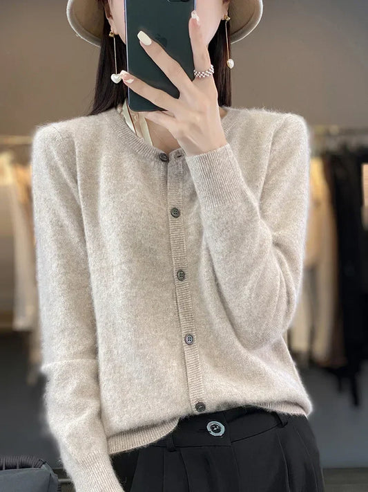 Frau in beigem Strickcardigan, hält Smartphone, trägt Hut und Ohrringe. Modetrend Herbst, elegante Damenmode, stilvoller Look.