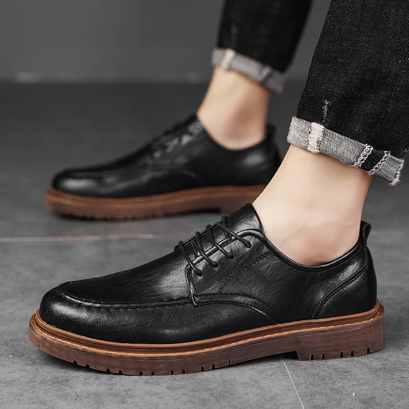 Schwarze Lederschuhe für Herren mit brauner Sohle, getragen zu hochgekrempelten Jeans. Elegante Herrenschuhe, ideal für Business und Freizeit.