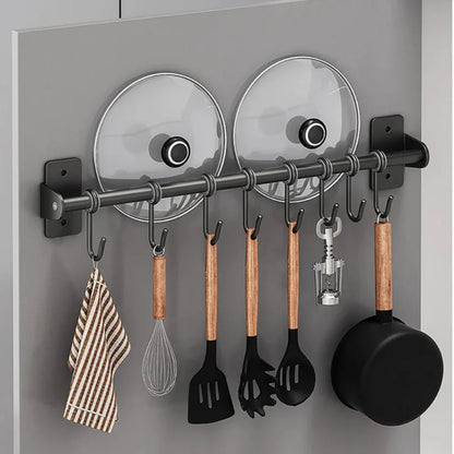 Küchenutensilienhalter mit Haken, Pfannen, Deckeln und Geschirrtuch an grauer Wand. Praktische Aufbewahrungslösung für Küchenzubehör.