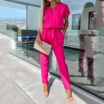 Frau in pinkem Jumpsuit mit beiger Clutch vor modernem Glasgebäude. Sommermode, eleganter Look, stilvolle Damenbekleidung, trendige Outfits.