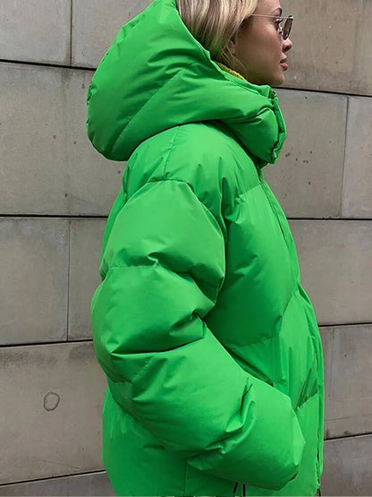 Frau in grüner Daunenjacke mit Kapuze vor Betonwand, Wintermode, warme Outdoor-Bekleidung, stilvolle Damenjacke, modische Wintertrends.
