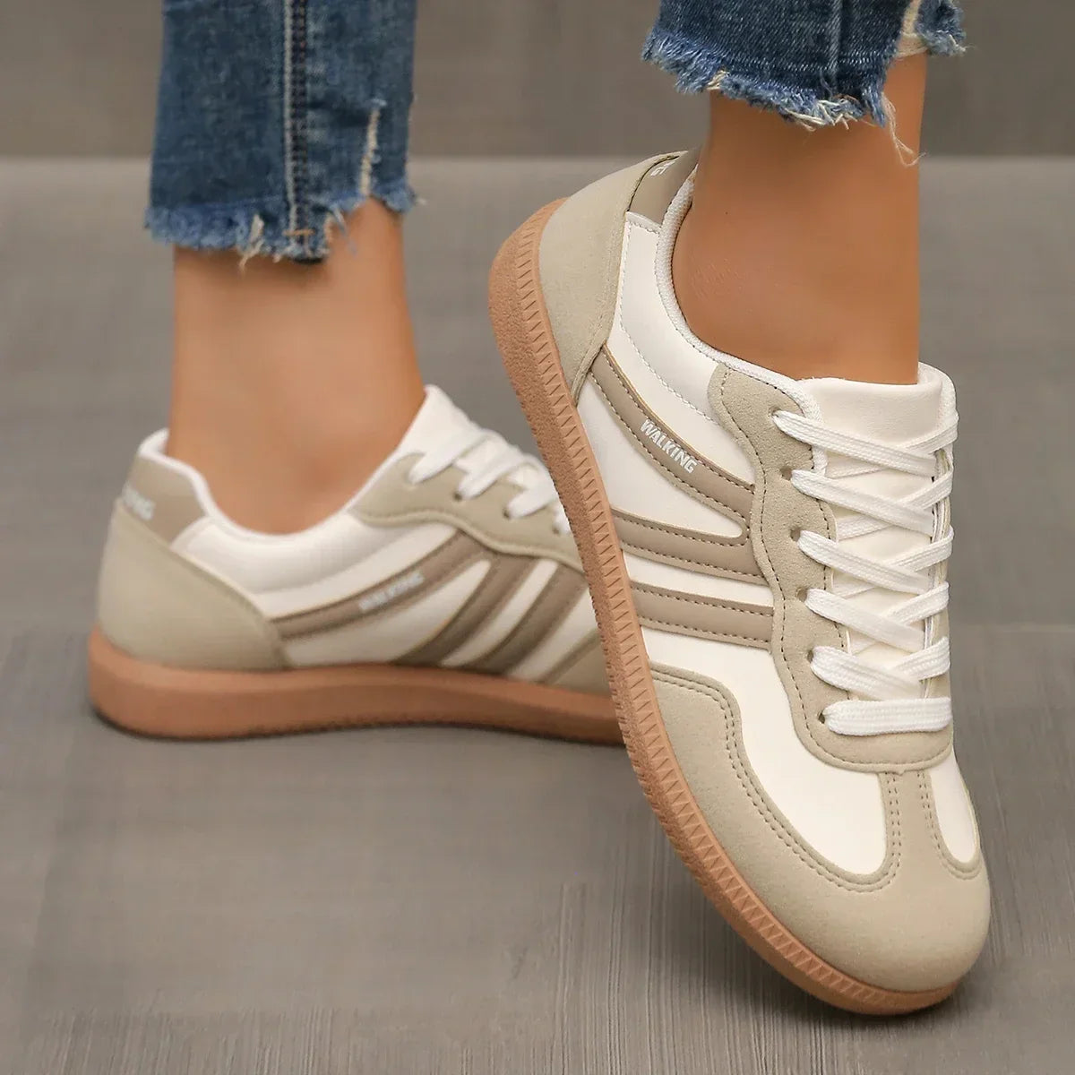 Damen Sneaker in Beige und Weiß, mit Gummisohle und Schnürsenkeln, getragen auf grauem Boden. Modische Freizeitschuhe, ideal für den Alltag.