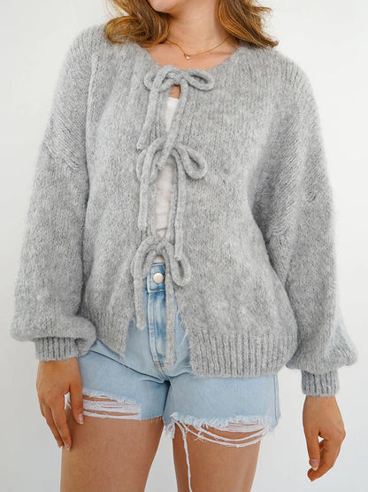 Frau trägt grauen Strickpullover mit Schleifen, kombiniert mit zerrissenen Jeansshorts. Modetrend, gemütlicher Look, Herbstmode.