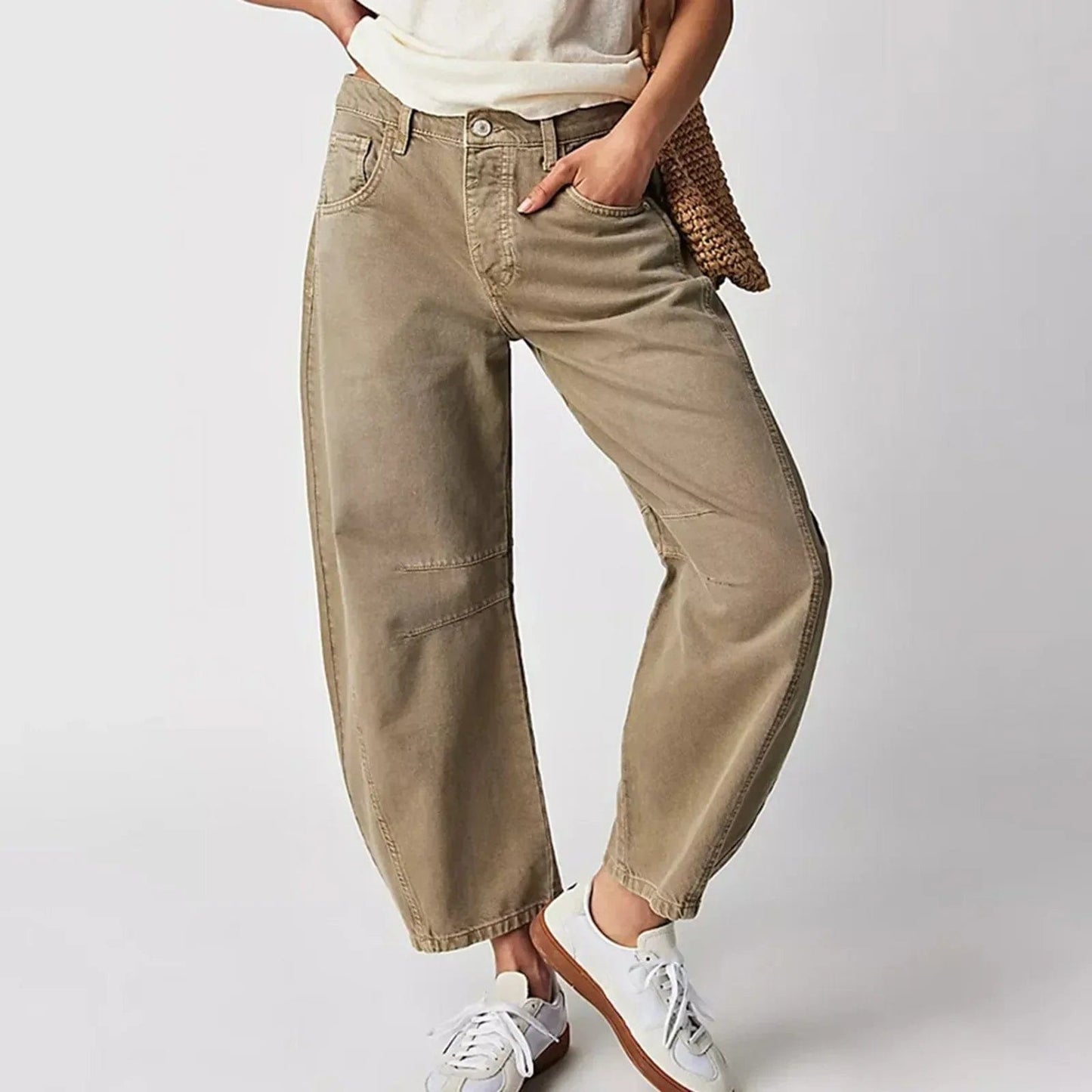Damen in beigen Baggy-Jeans und weißen Sneakers, lässiger Look, Hand in der Tasche, modische Freizeitkleidung, neutraler Hintergrund.