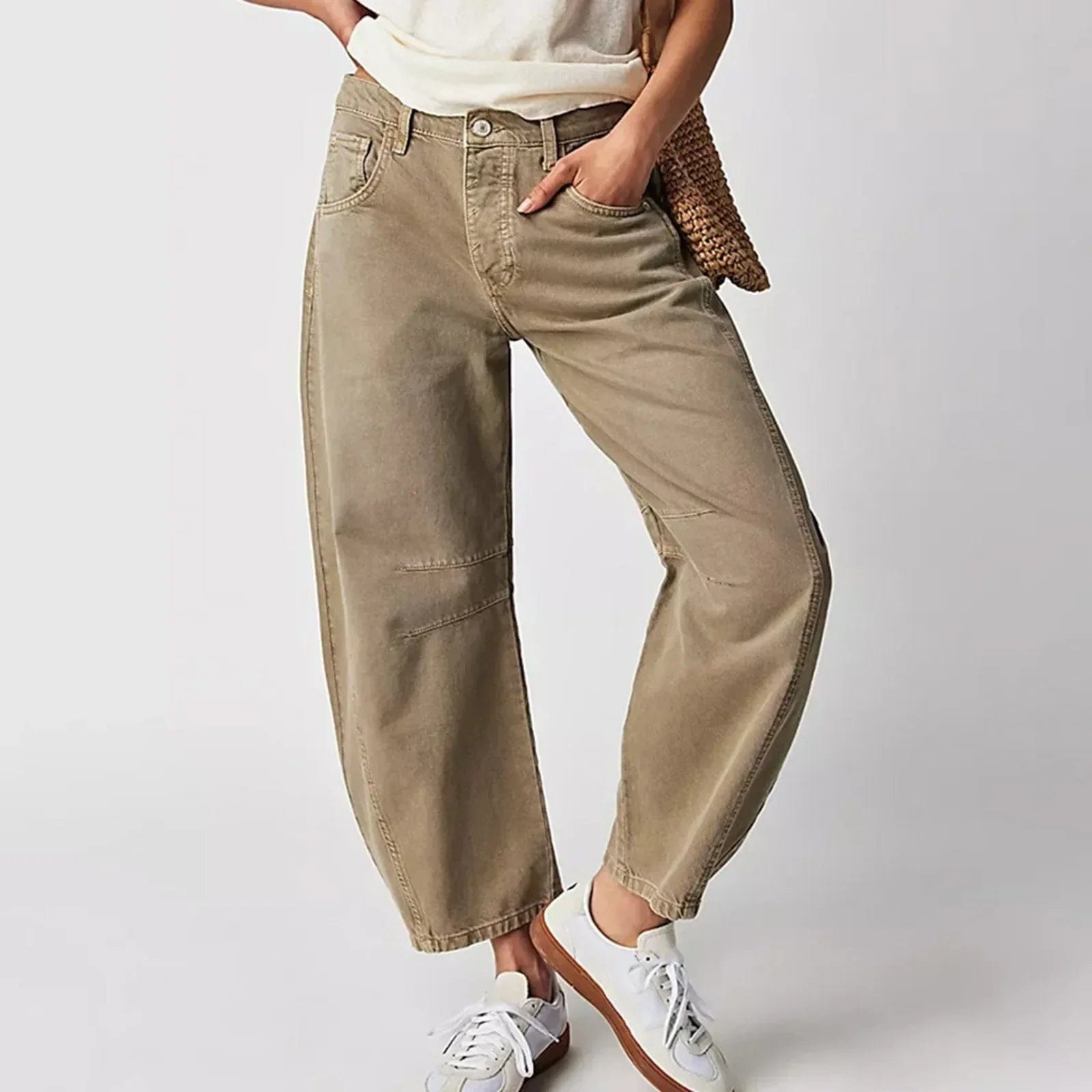 Damen in beigen Baggy-Jeans und weißen Sneakers, lässiger Look, Hand in der Tasche, modische Freizeitkleidung, neutraler Hintergrund.