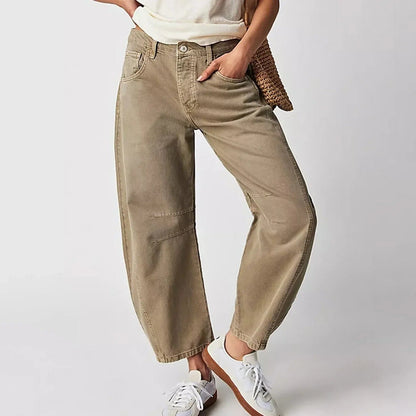 Damen in beigen Baggy-Jeans und weißen Sneakers, lässiger Look, Hand in der Tasche, modische Freizeitkleidung, neutraler Hintergrund.