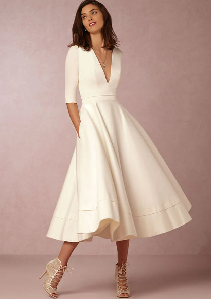Frau in elegantem, cremefarbenem A-Linien-Kleid mit V-Ausschnitt und halblangen Ärmeln, kombiniert mit Schnürstiefeletten. Perfekt für Hochzeiten.
