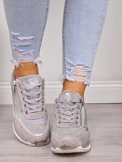 Graue Glitzersneaker an Füßen mit zerrissenen Jeans auf Holzboden. Modische Damen-Sneaker, glänzend, lässiger Stil, trendige Schuhe.