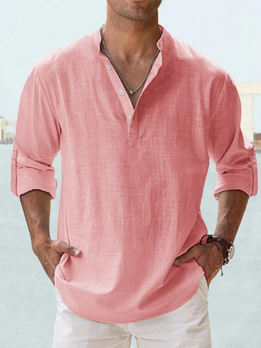 Mann in rosa Leinenhemd mit Stehkragen und Knopfleiste, lässig hochgekrempelte Ärmel, kombiniert mit weißer Hose, modisch und sommerlich.