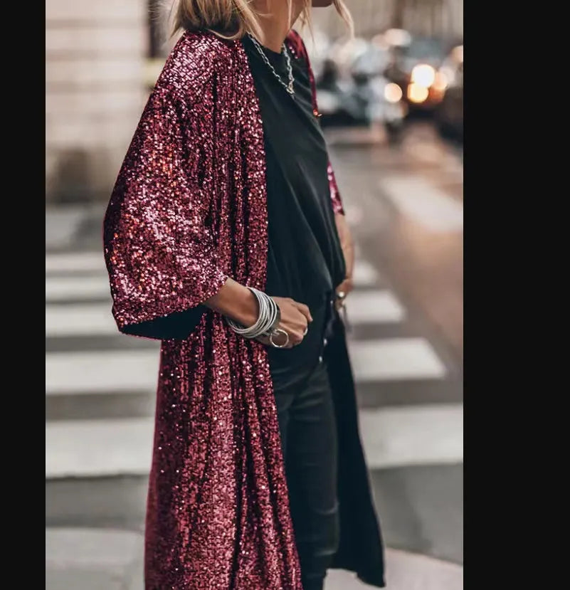 Frau in schwarzem Outfit mit glänzendem, rotem Paillettenmantel auf Straße. Modetrend, Streetstyle, glamouröser Look, urbane Mode.