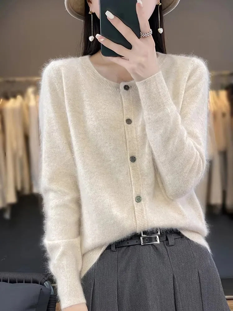 Dame in cremefarbenem Strickpullover mit Knopfleiste, grauer Hose und Hut, hält Smartphone. Modetrend, Herbstmode, eleganter Look.