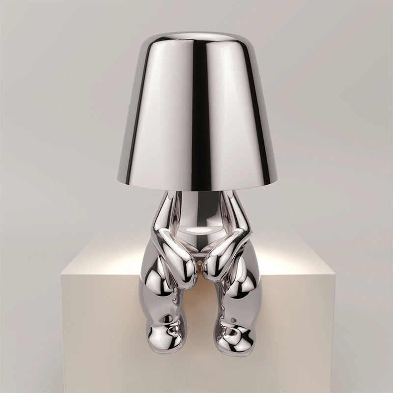 Silberne Designer-Tischlampe in menschlicher Form auf weißem Podest, modernes Interieur, stilvolle Beleuchtung, zeitgenössisches Design.