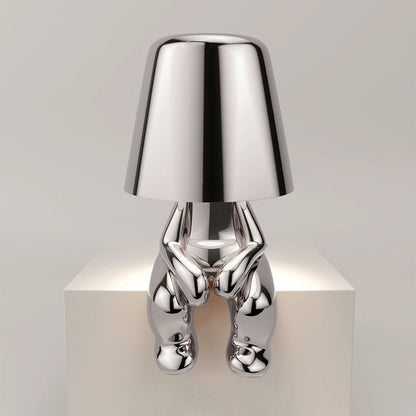 Silberne Designer-Tischlampe in menschlicher Form auf weißem Podest, modernes Interieur, stilvolle Beleuchtung, zeitgenössisches Design.