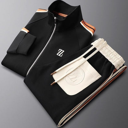 Schwarzer Designer-Trainingsanzug mit weißem Logo, Reißverschlussjacke und elastischer Hose, modisch und sportlich, auf grauem Hintergrund.