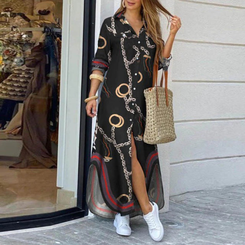 Frau in langem, gemustertem Kleid mit Ketten- und Kreisdesign, trägt Strohtasche und weiße Sneaker, steht vor einem Schaufenster.