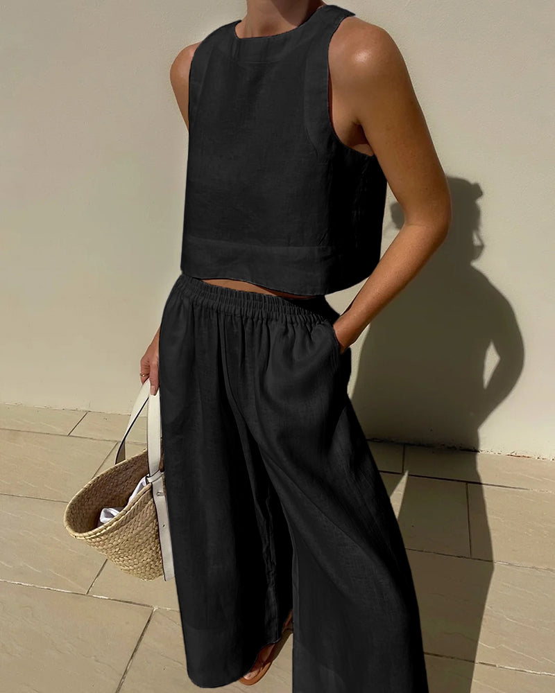 Frau in schwarzem Leinen-Zweiteiler mit ärmellosem Top und weiter Hose, hält Strohtasche. Sommermode, minimalistischer Stil, elegantes Outfit.