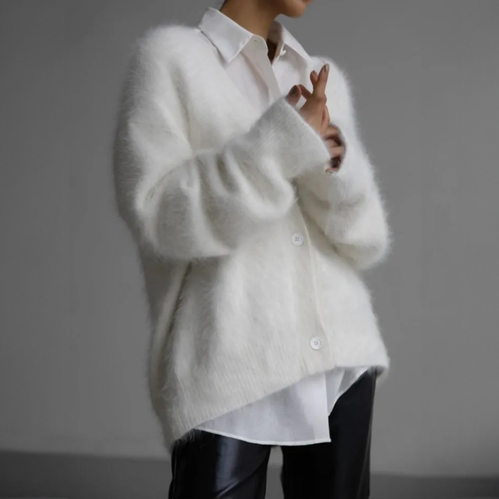 Frau in weißem, flauschigem Cardigan und weißer Bluse, kombiniert mit schwarzer Lederhose. Elegante, minimalistische Mode.