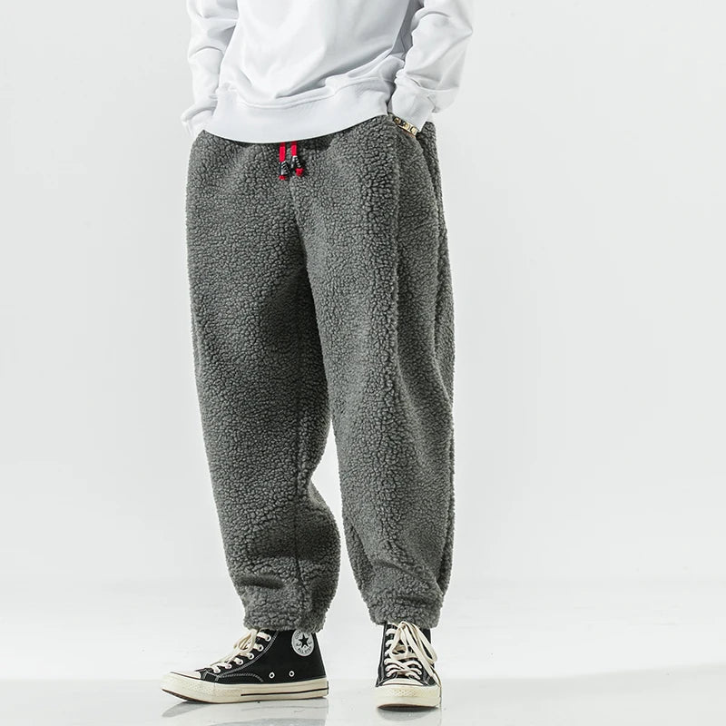 Graue Fleece-Jogginghose, lässig geschnitten, kombiniert mit weißen Sneakers und weißem Oberteil. Bequem, modisch, ideal für Freizeitkleidung.