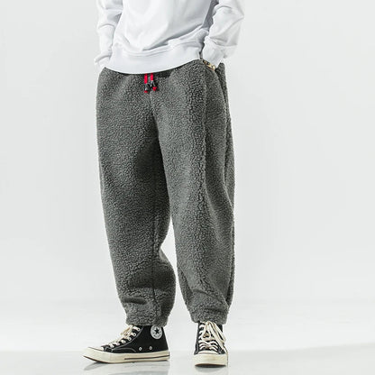 Graue Fleece-Jogginghose, lässig geschnitten, kombiniert mit weißen Sneakers und weißem Oberteil. Bequem, modisch, ideal für Freizeitkleidung.