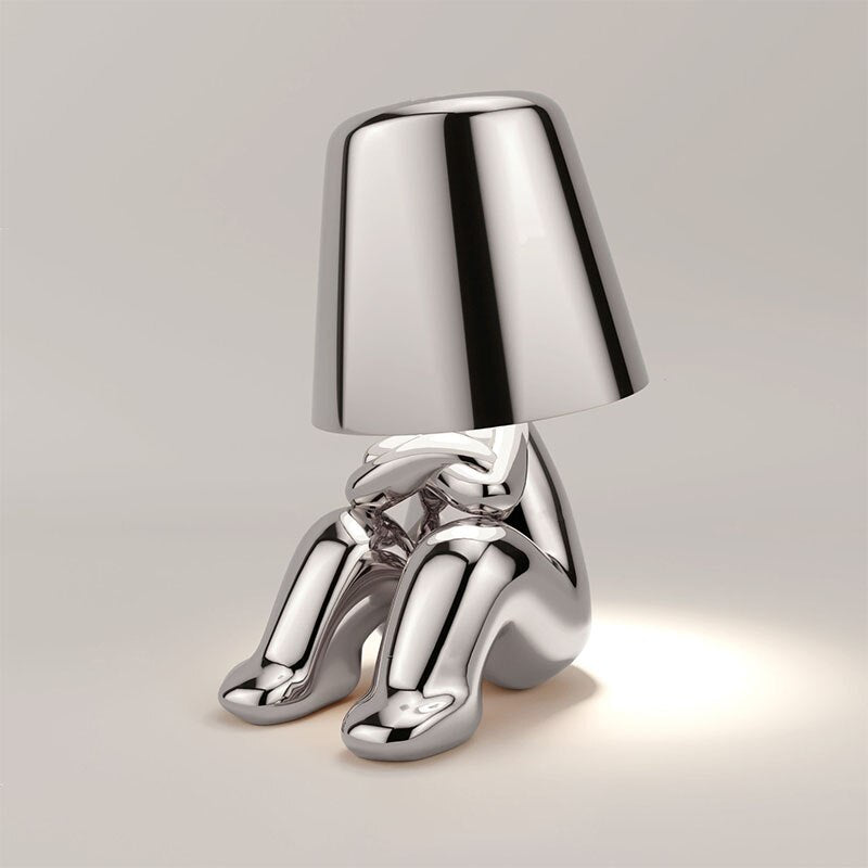 Silberne Designer-Tischlampe in Form einer sitzenden Figur, modernes Innendekor, stilvolle Beleuchtung, minimalistisches Design, glänzende Oberfläche.