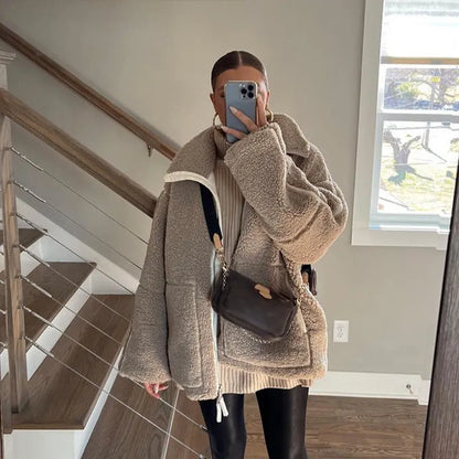 Frau in übergroßer Teddyjacke, schwarzer Lederhose, mit Handy vor Spiegel. Wintermode, gemütlicher Look, Selfie, Treppenhaus.