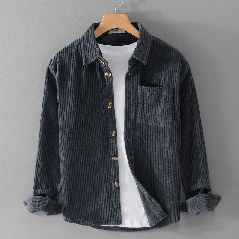 Graues Cordhemd mit Holzknöpfen, über weißem T-Shirt, auf Holzkleiderbügel vor grauer Wand. Herrenmode, lässiger Stil, Herbstbekleidung.