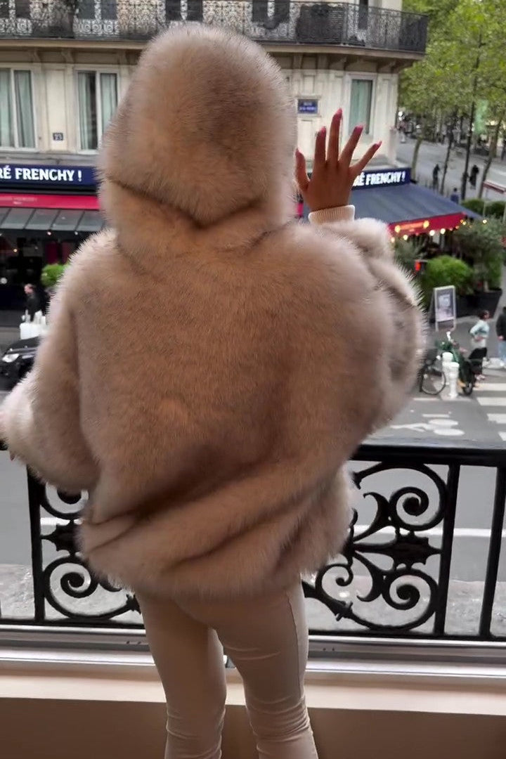 Person in weißem Pelzmantel auf Balkon, blickt auf Pariser Straße. Elegante Mode, Stadtansicht, urbane Szene, stilvolle Kleidung, Paris.