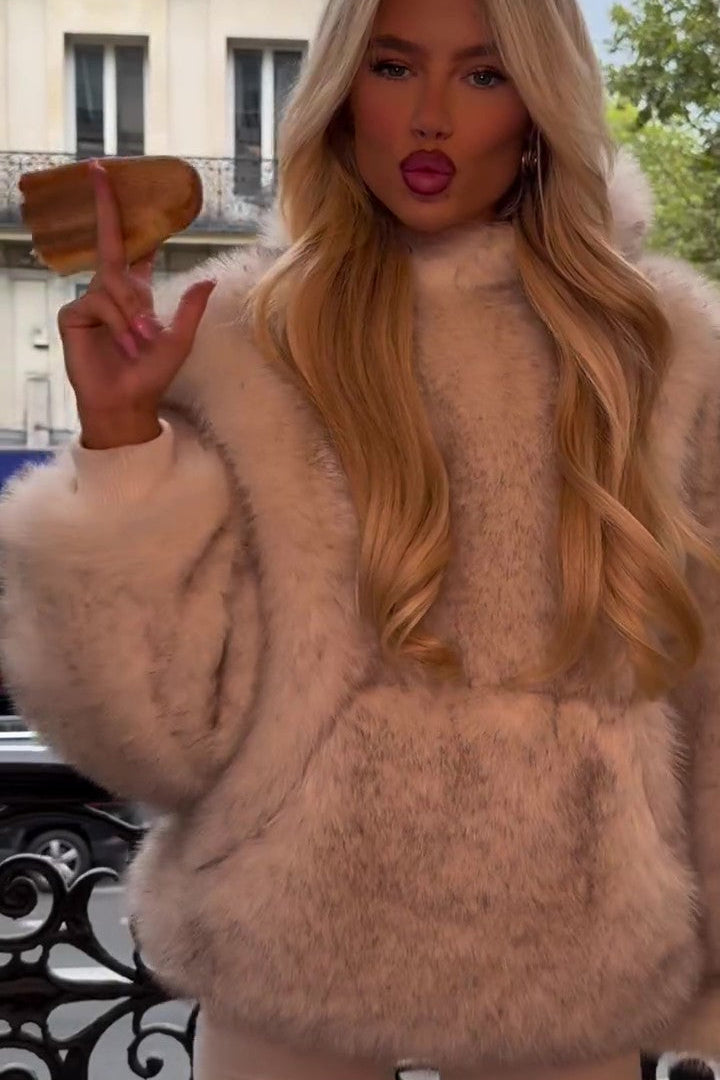 Blonde Frau in luxuriösem, cremefarbenem Pelzmantel posiert auf Balkon, hält Gebäck. Elegante Mode, Herbsttrends, Stadtblick, stilvolle Kleidung.