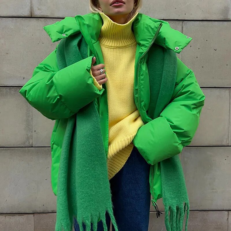 Frau in grüner Daunenjacke und gelbem Rollkragenpullover vor Betonwand. Wintermode, warme Kleidung, modischer Streetstyle.