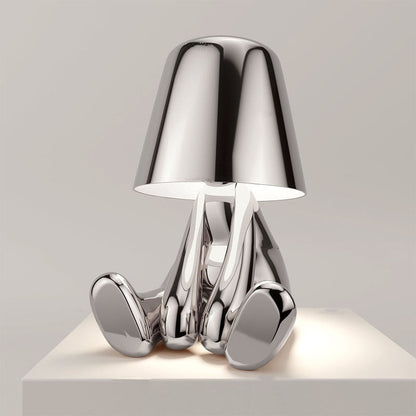 Silberne Designer-Tischlampe in Form einer sitzenden Figur, modernes minimalistisches Design, glänzende Metalloberfläche, stilvolle Wohnkultur.