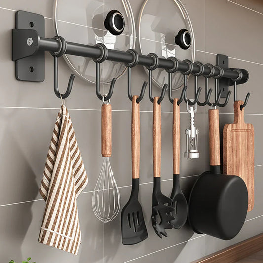 Schwarze Küchenleiste mit Haken, an denen Kochutensilien aus Holz und Metall hängen, inklusive Pfanne, Schneebesen, Schöpfkelle und Geschirrtuch.