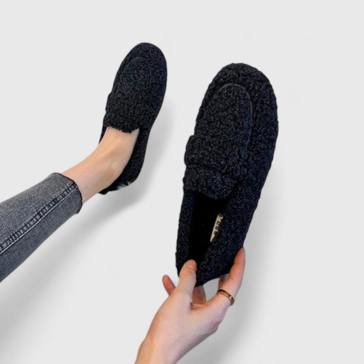 Schwarze, flauschige Hausschuhe an Füßen, getragen von Person in Jeans. Bequeme, warme Slipper für Damen. Ideal für gemütliche Winterabende.