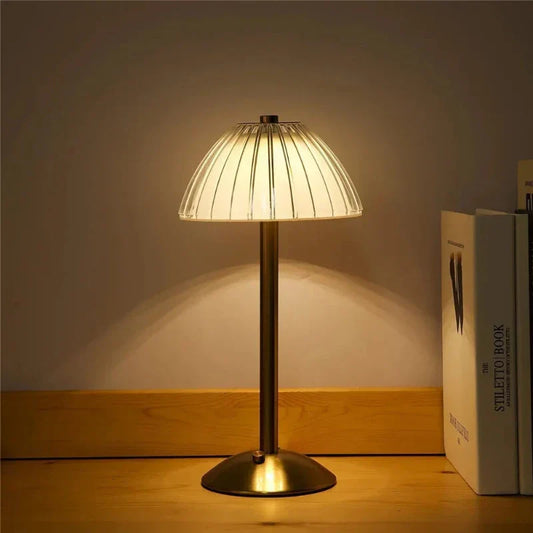 Klassische Tischlampe mit Messingfuß und gefaltetem Lampenschirm, beleuchtet auf Holzoberfläche, ideal für stilvolle Wohn- und Schlafzimmerbeleuchtung.