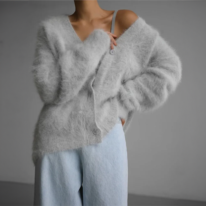 Frau in grauem, flauschigem Strickcardigan und hellblauer Hose vor grauem Hintergrund. Modetrend, gemütlicher Look, Herbstmode.