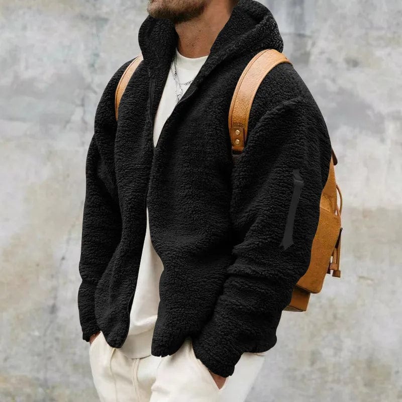 Mann in schwarzer Fleecejacke mit braunem Rucksack vor grauer Wand. Modischer Herbst-Look, lässiger Stil, Outdoor-Bekleidung.