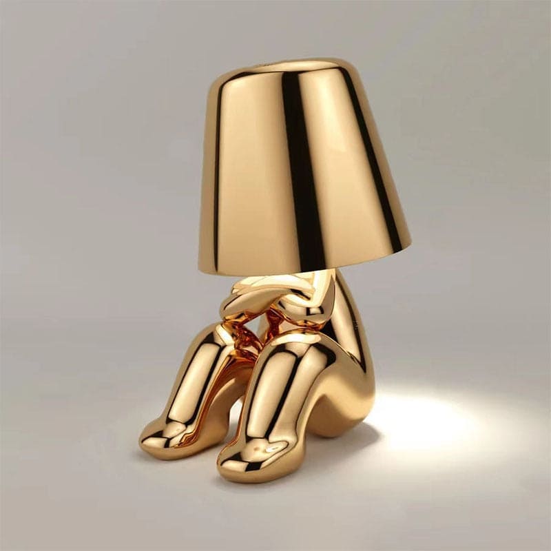 Goldene Tischlampe in Form einer sitzenden Figur, modernes Design, warmes Licht, stilvolle Wohnkultur, einzigartige Beleuchtungslösung.