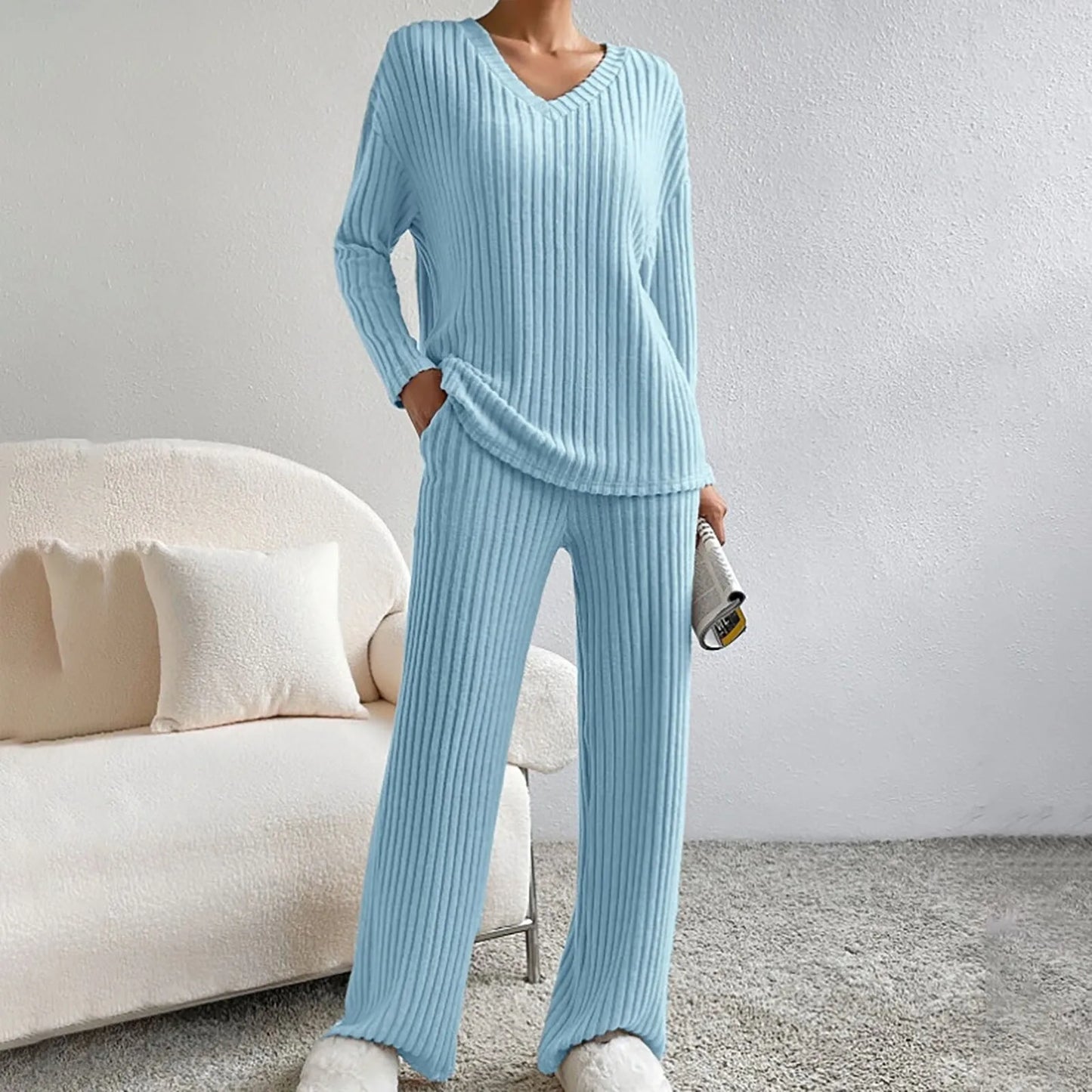 Damen in hellblauem Strick-Pyjama-Set, gemütlich auf grauem Teppich stehend, mit beigem Sofa im Hintergrund. Perfekt für entspannte Abende zu Hause.