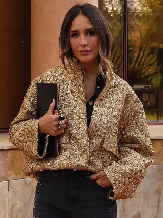 Frau in goldener Paillettenjacke, hält schwarze Clutch, steht vor Gebäude. Modetrend, glamouröser Look, stilvolle Abendgarderobe.
