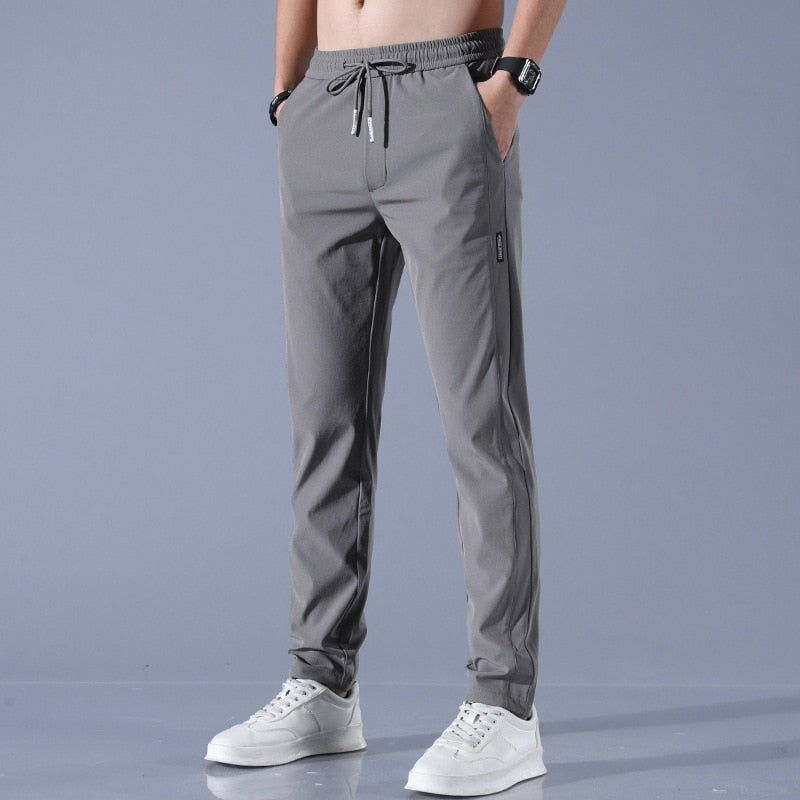 Graue Jogginghose für Herren, elastischer Bund, Kordelzug, seitliche Taschen, sportlich, bequem, kombiniert mit weißen Sneakers, modisch.
