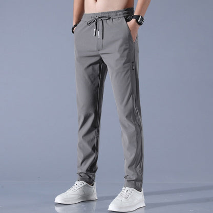 Graue Jogginghose für Herren, elastischer Bund, Kordelzug, seitliche Taschen, sportlich, bequem, kombiniert mit weißen Sneakers, modisch.