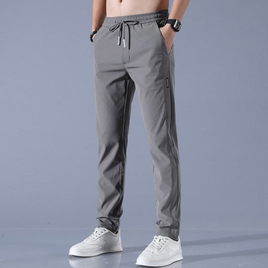 Graue Jogginghose für Herren, elastischer Bund, Kordelzug, seitliche Taschen, sportlich, bequem, kombiniert mit weißen Sneakers, modisch.
