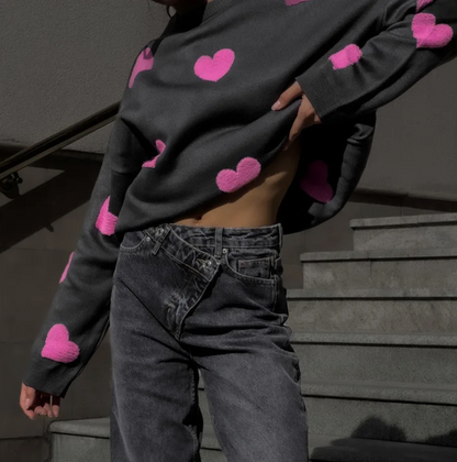 Grauer Pullover mit pinken Herzen, kombiniert mit hoch taillierten, überkreuzten Jeans. Modetrend, Streetstyle, Herbstmode.