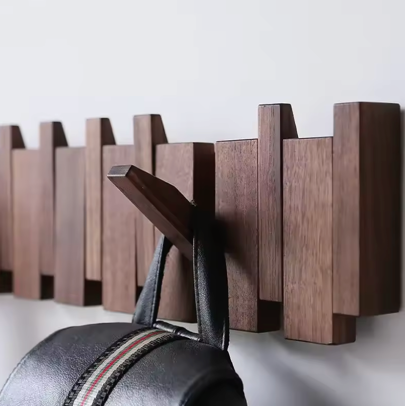 Moderne Wandgarderobe aus Holz mit klappbaren Haken, an der eine schwarze Tasche hängt. Stilvolle Aufbewahrungslösung für Flur oder Eingangsbereich.
